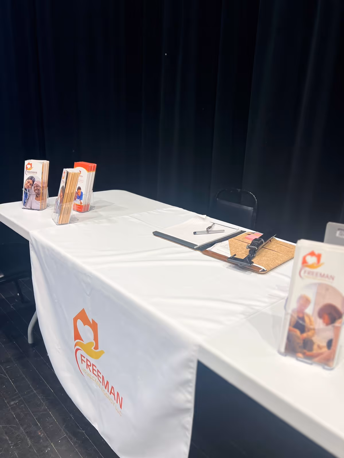 Table with Freeman Homecare Agency brochures, a clipboard, and pamphlet stands against a dark backdrop.