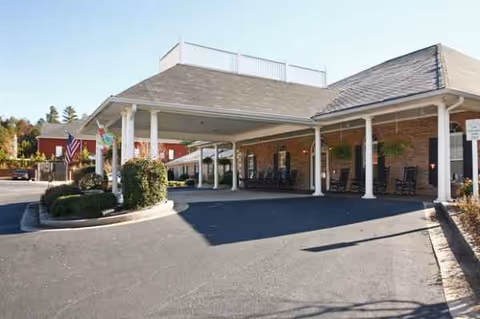 Covered entrance of Cedarhurst of Oakwood senior living with columns, chairs, and parking area.