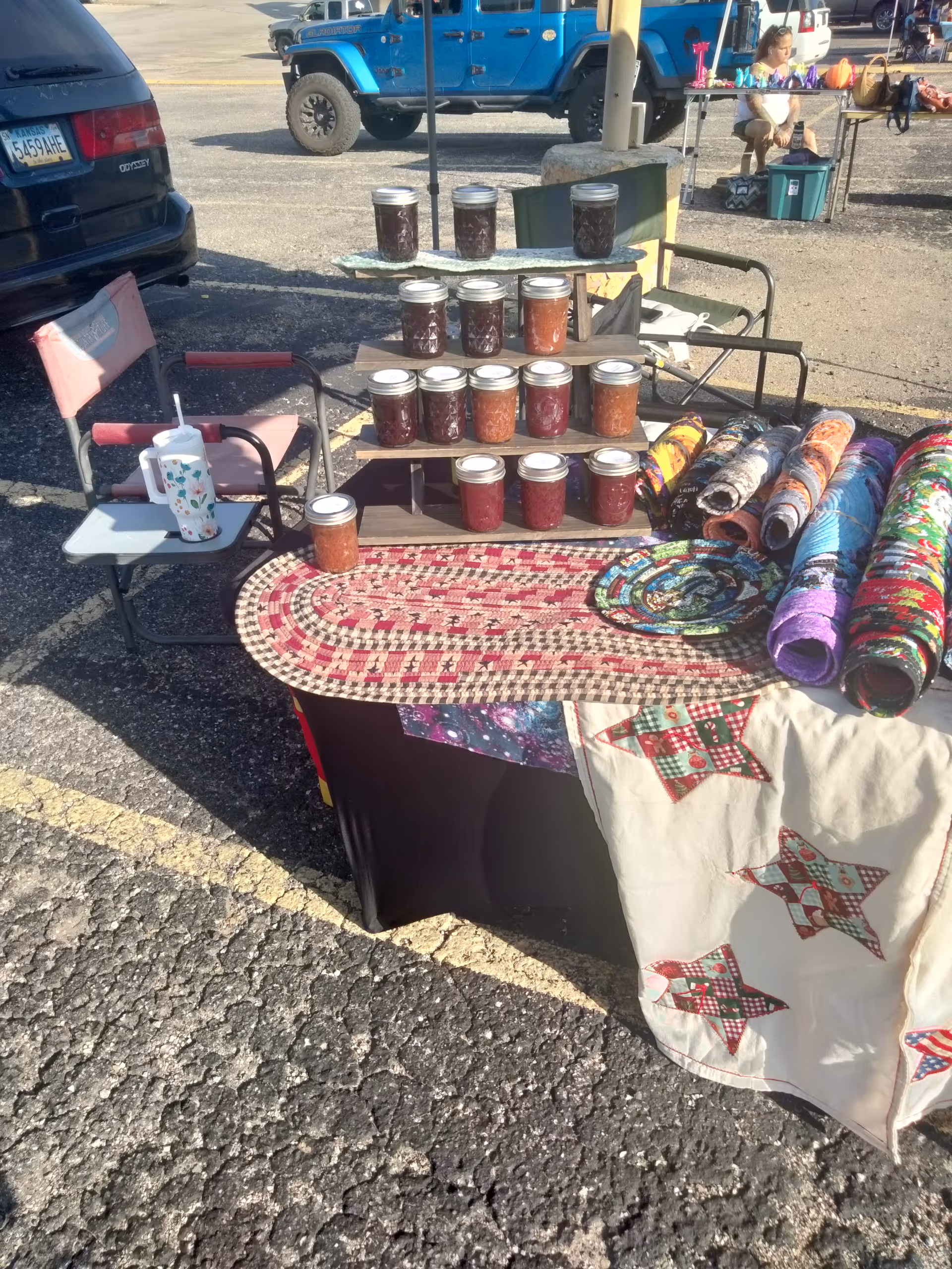 Outdoor market stall with jars of jam displayed on shelves and mats.
