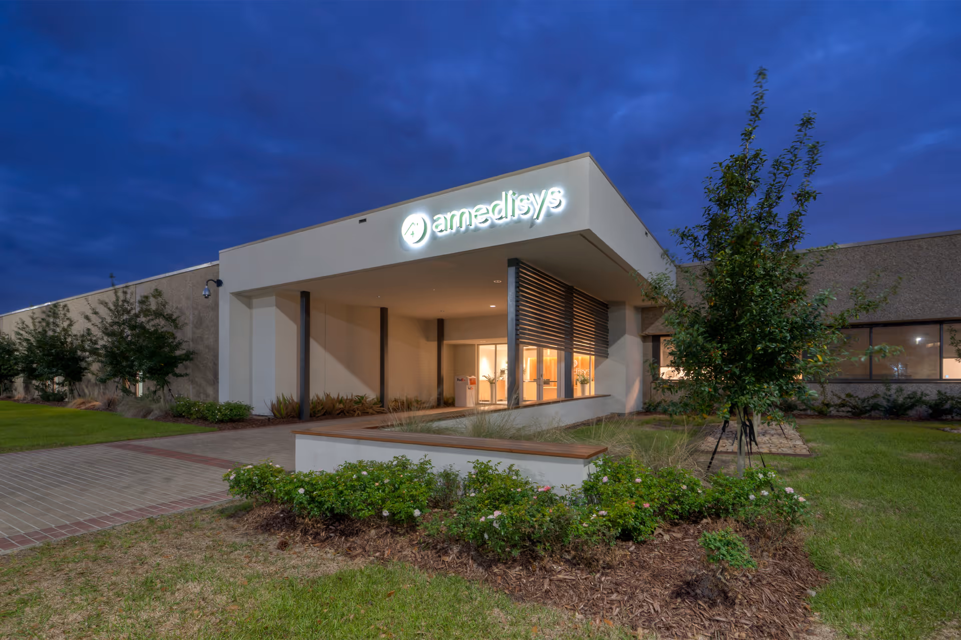 Amedisys Corporate Headquarters building exterior with illuminated sign and landscaped entrance at dusk.
