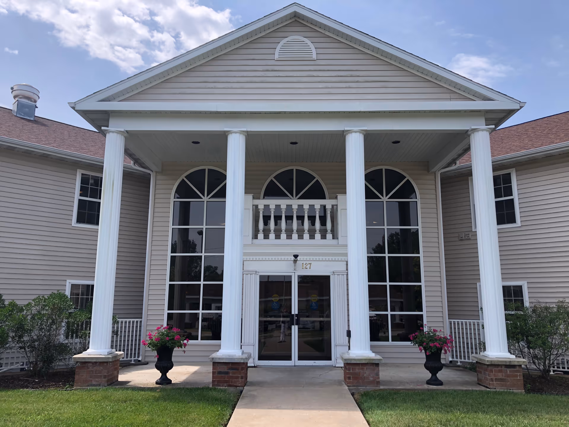 Front entrance of a beige retirement community building with tall white columns and arched windows.