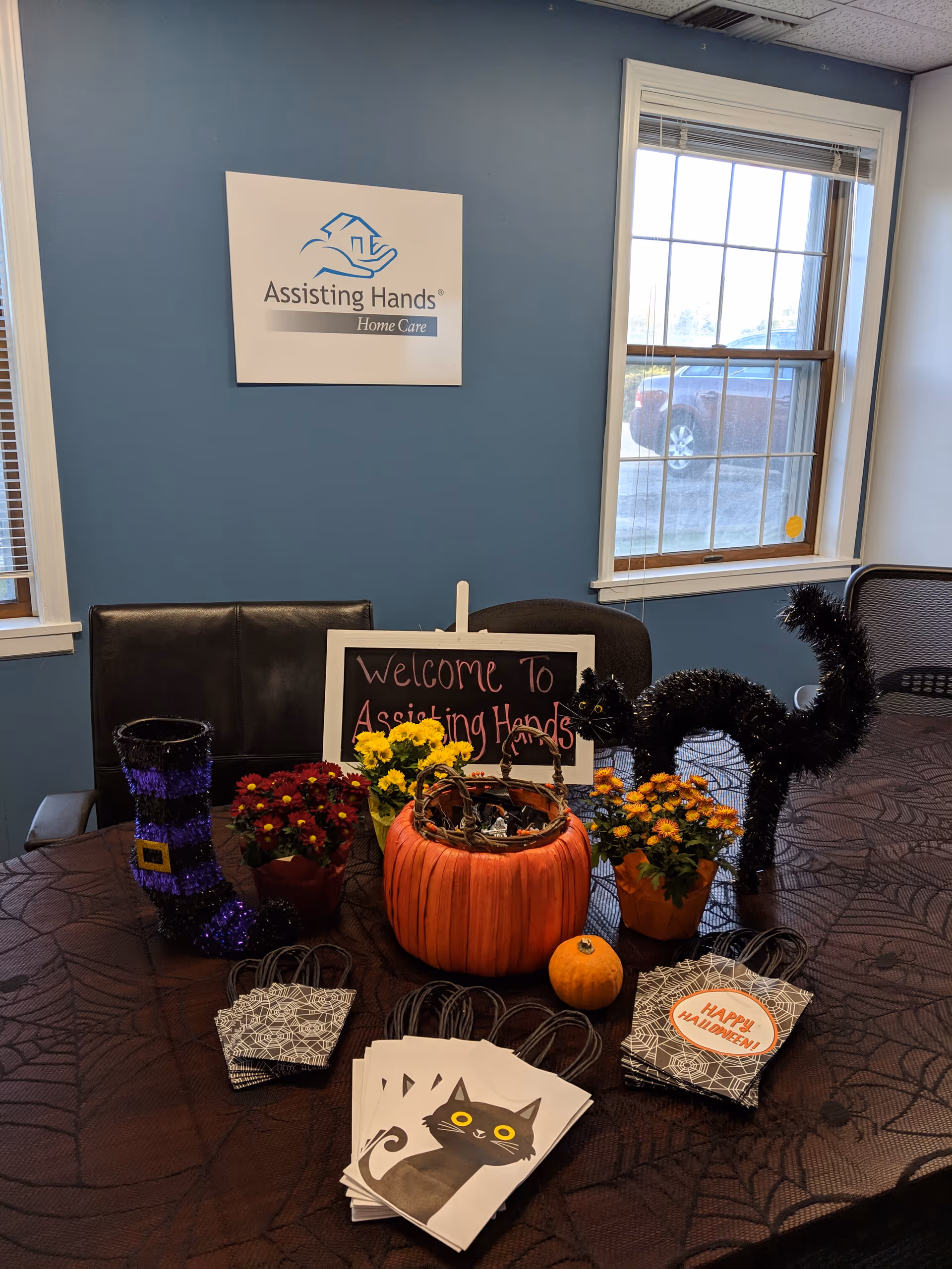 Reception area with blue wall, logo sign, decorated table, pumpkins, flowers, and Halloween cards.