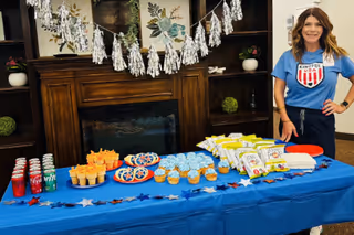 A woman in a Kindful Health shirt stands beside a snack table in a living room.