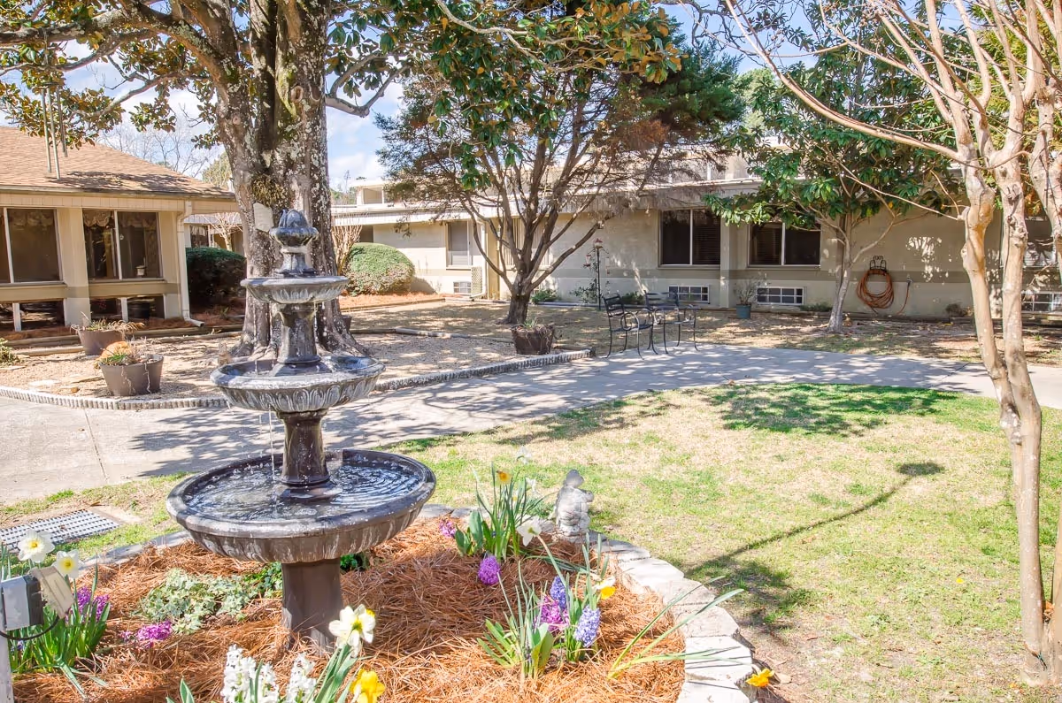 Courtyard with a tiered fountain, flowering garden, and benches in front of a residential building.