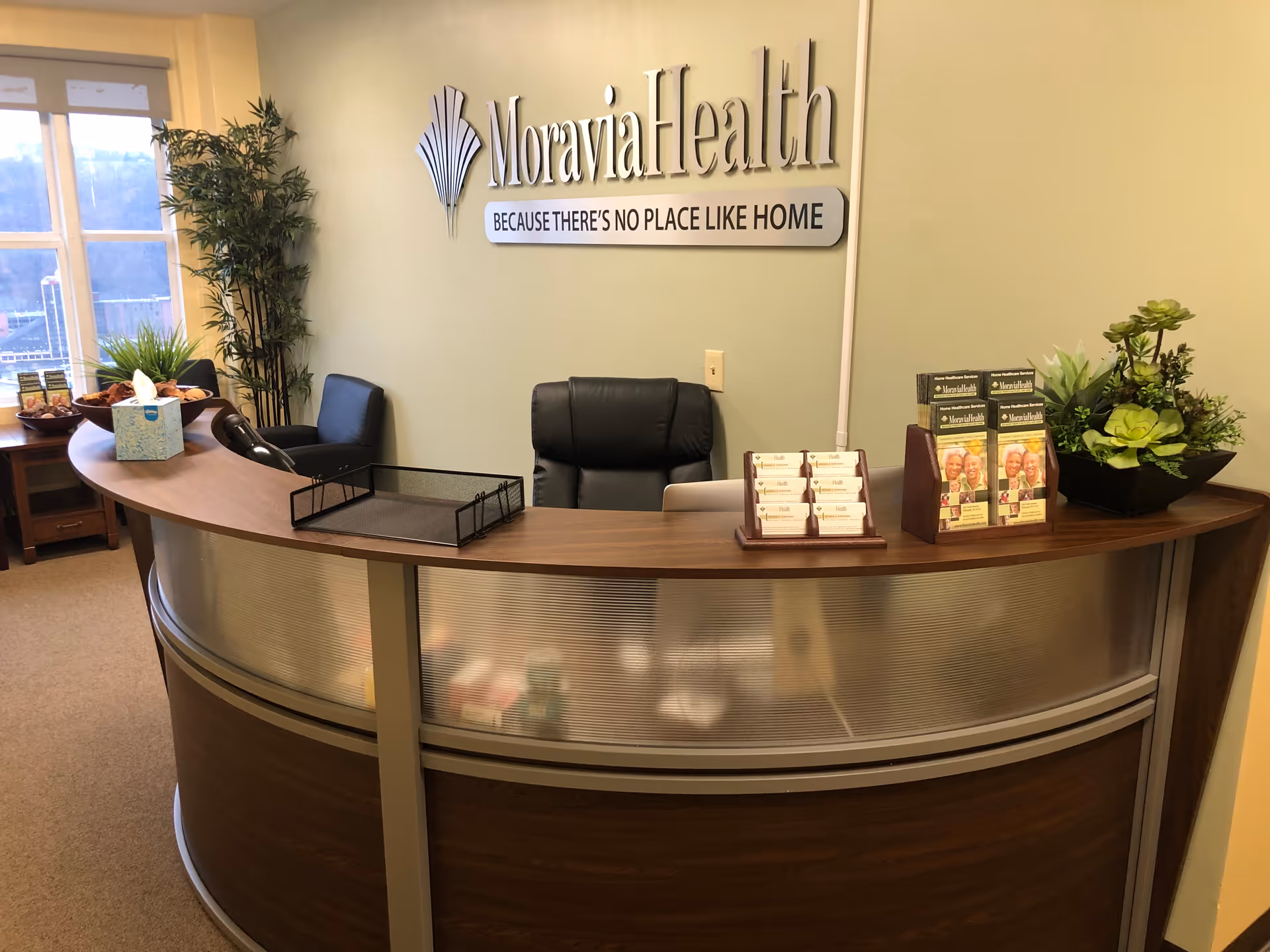 Curved wooden reception desk in a Moravia Health Pittsburgh lobby with plants and sign.