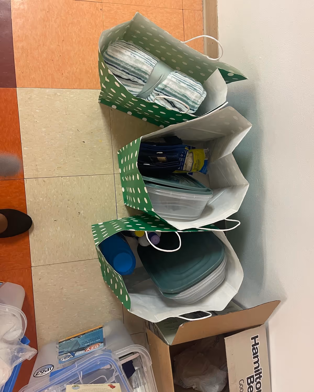 Green polka dot bags hold towels and supplies stacked against a wall in a hallway.