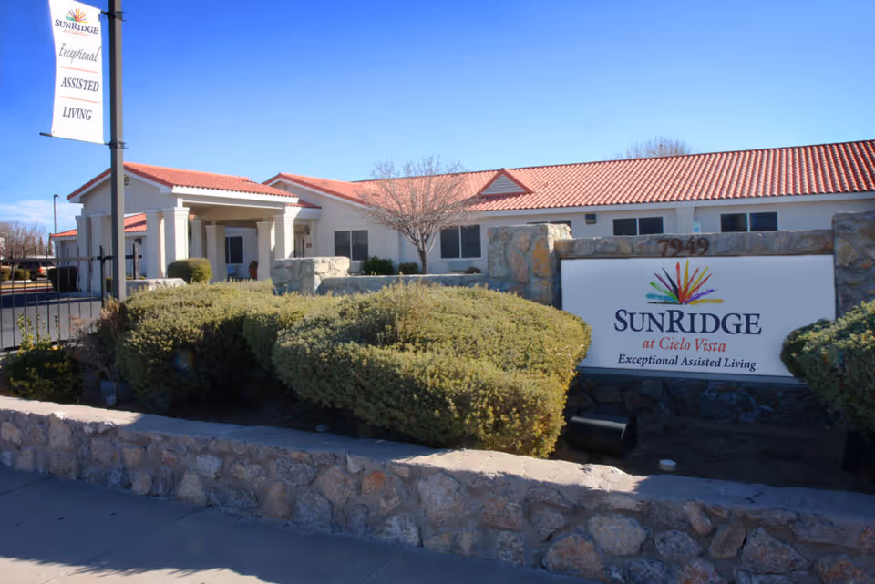 Front exterior of a single-story assisted living building with a stone wall, landscaping, and a large sign reading 'SunRidge at Cielo Vista'.