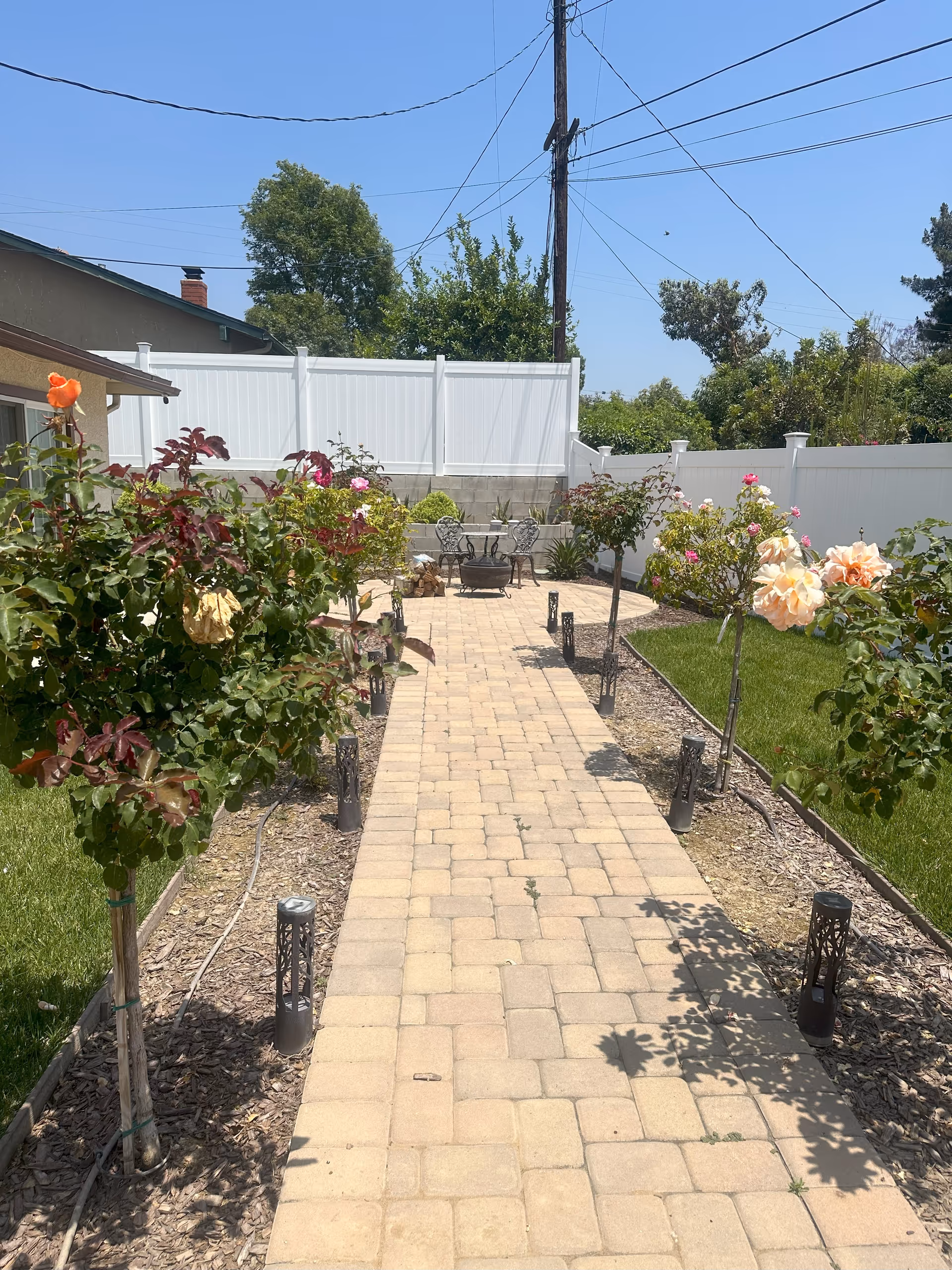 A paved garden path leads to a seating area in a rose-filled outdoor courtyard.
