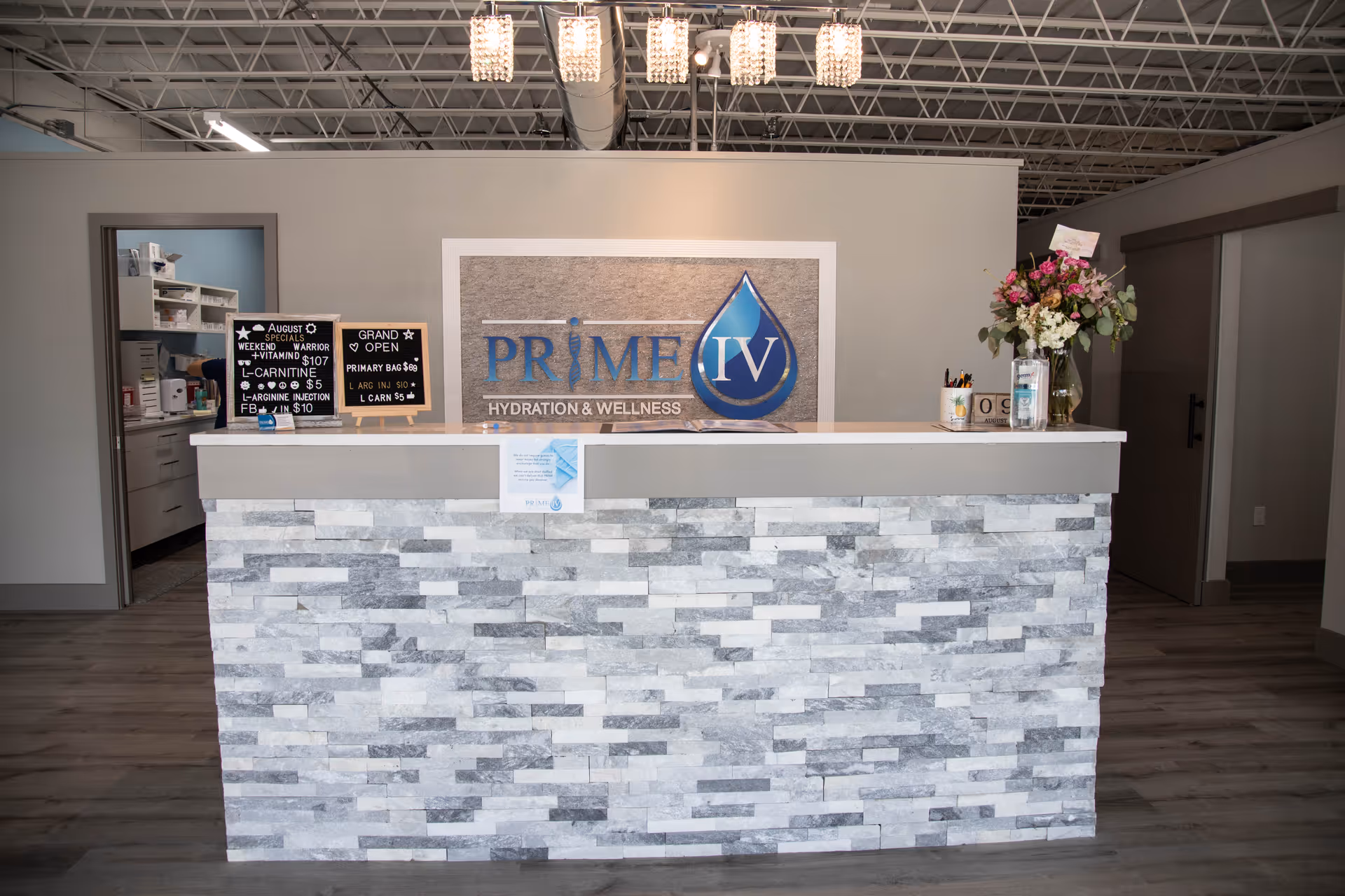 Reception desk with stone facade, signage reading Prime IV Hydration and Wellness, and a floral arrangement.
