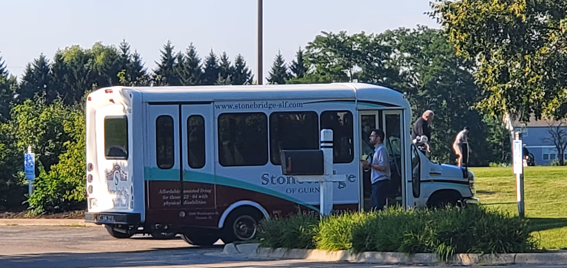 Stonebridge of Gurnee shuttle bus parked outdoors with two people nearby in a grassy lot.