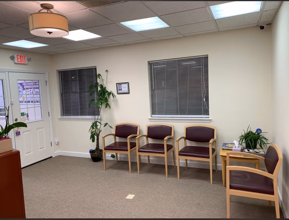 A waiting area with four burgundy chairs, a small table, plants, and an exit door.