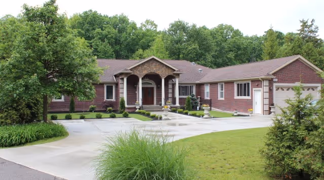 Front exterior view of a single-story brick building with a covered entrance supported by columns, surrounded by a well-maintained lawn, shrubs, and trees under a clear sky.
