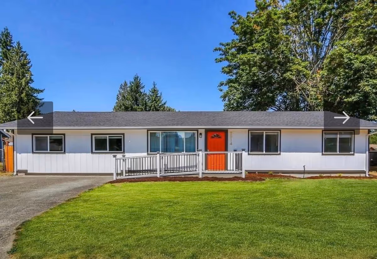 Single-story white building with red front door and ramp, set on green lawn.