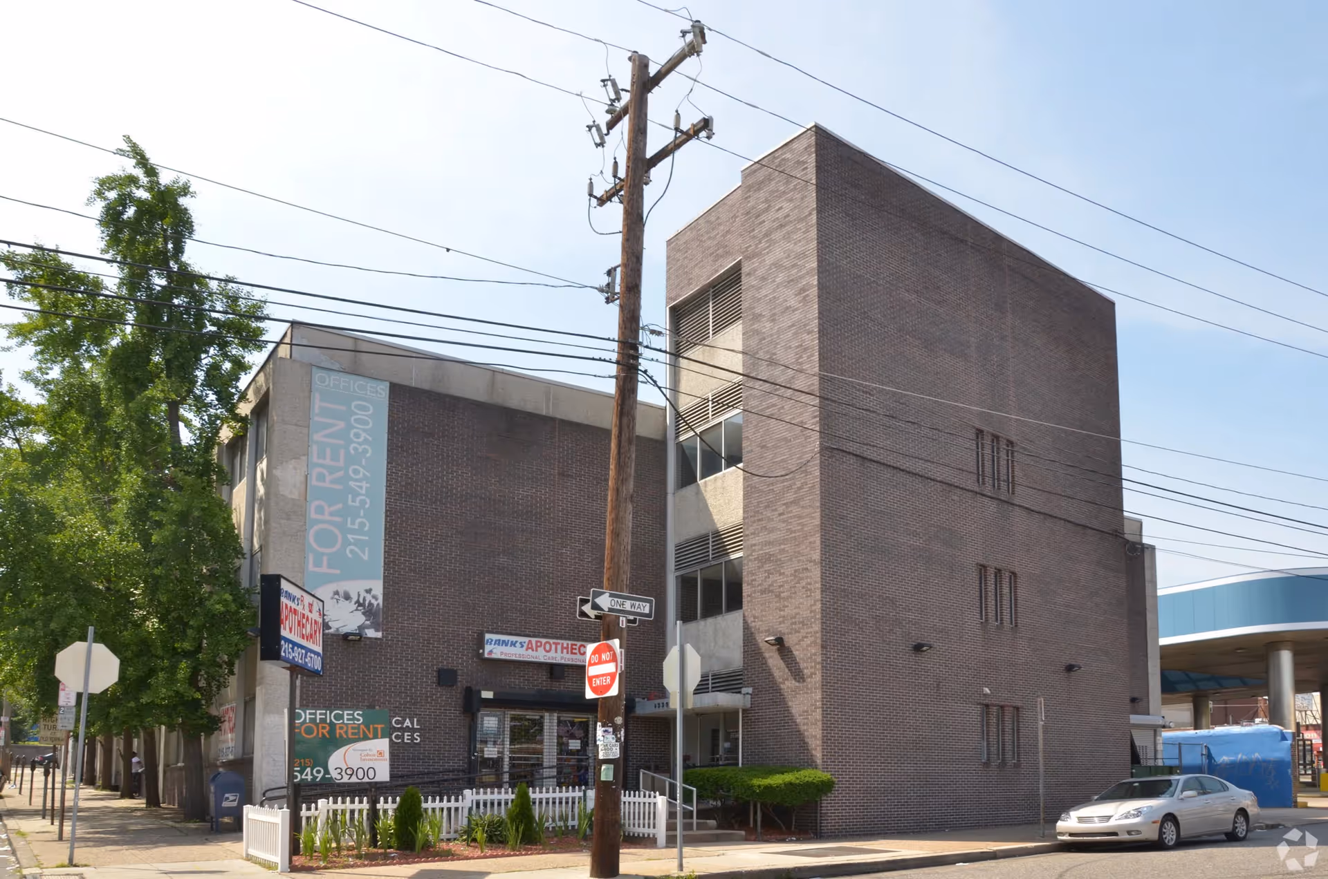 Brick multi-story building on a city street with power lines and for-rent signs.