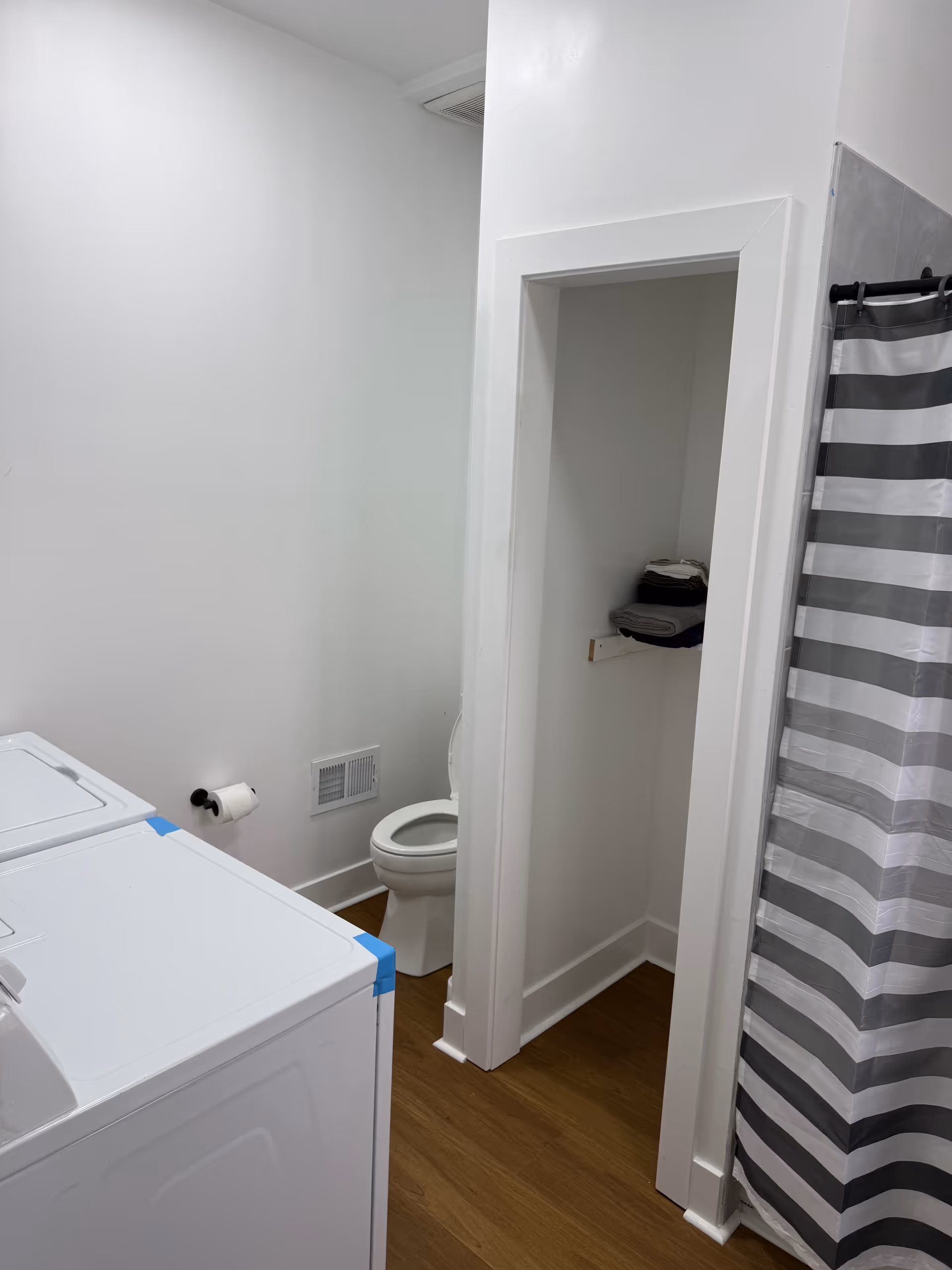 Small bathroom with a toilet alcove, striped shower curtain, and a washer/dryer in white walls