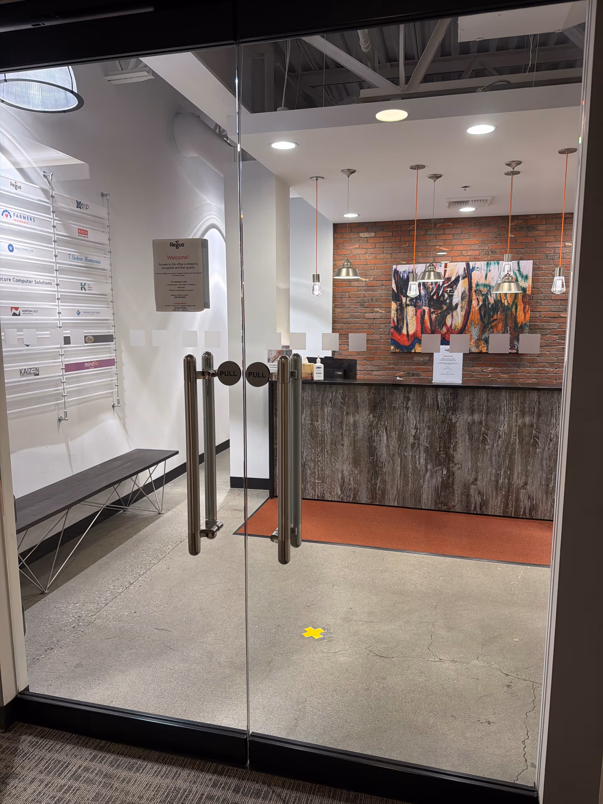 Glass double doors lead to a reception area with brick accent wall and abstract art.