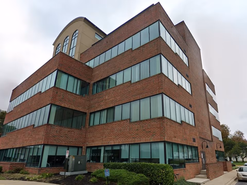 Brick, multi-story senior living facility with large glass windows and landscaped surroundings.