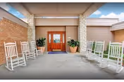 The front entrance of Senior Care Beltline features white rocking chairs and potted plants.