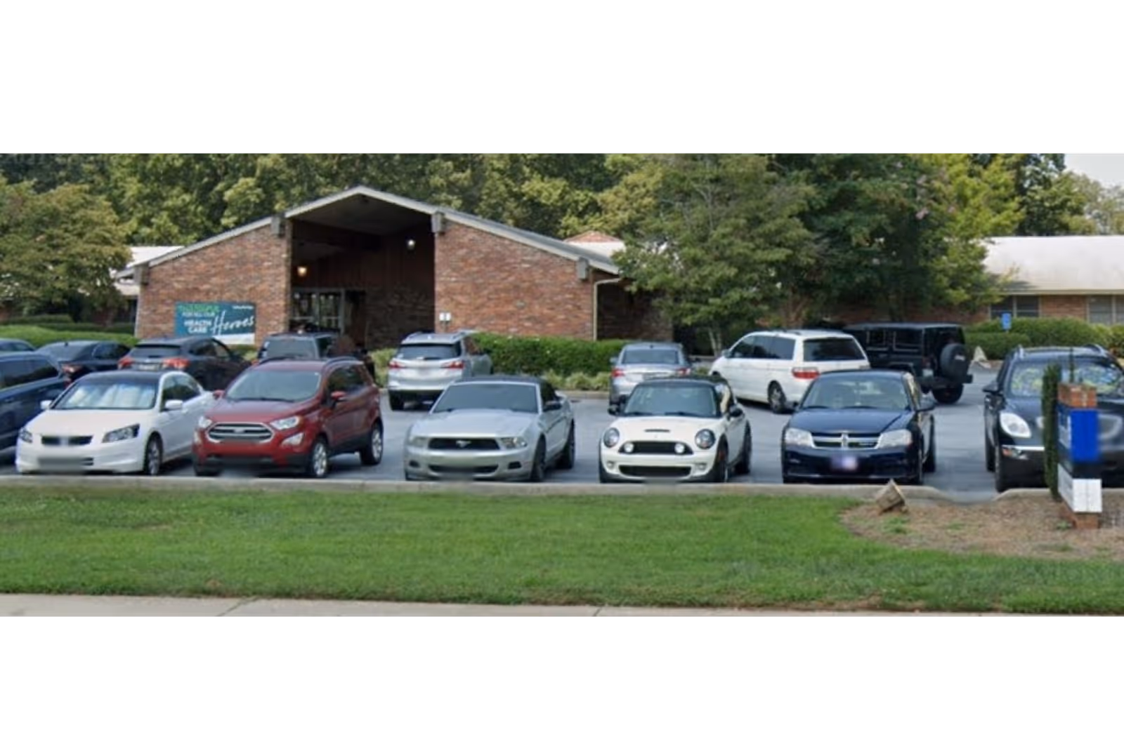 Front exterior of Reedy River Post Acute with a parking lot and trees.