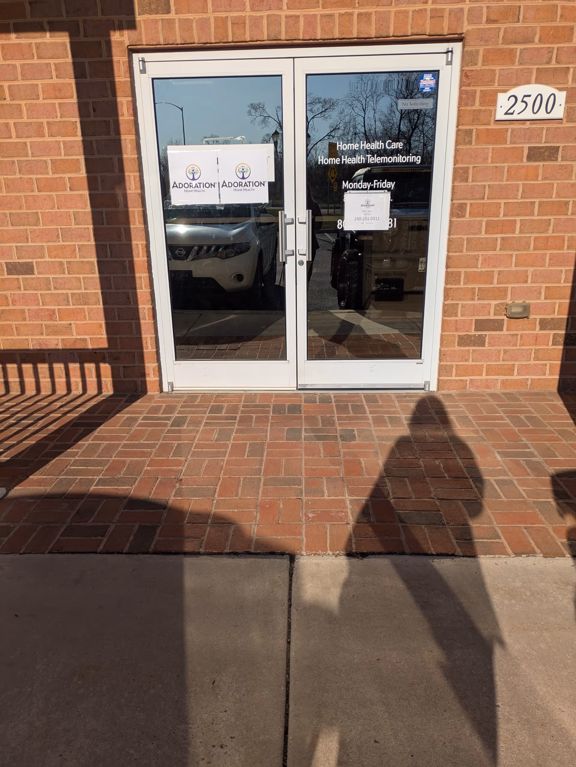 Glass double doors with Adoration Home Health signage, brick exterior, and brick sidewalk.