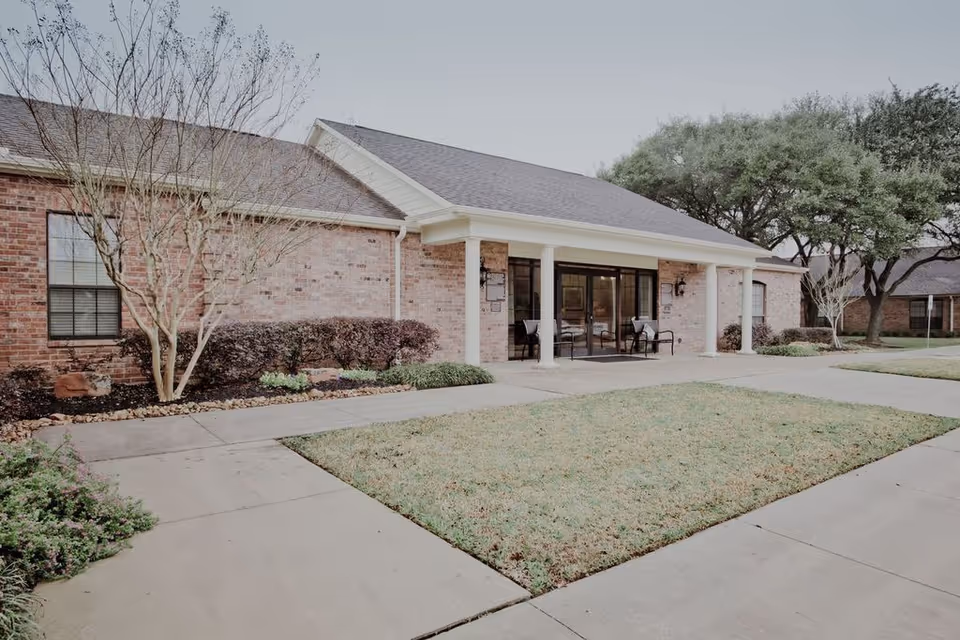 Front view of a brick senior living facility with a covered entrance and outdoor seating.