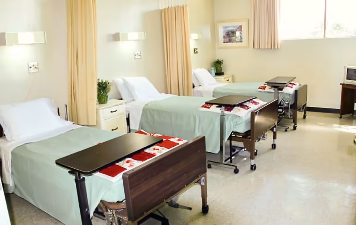 Multiple hospital beds in a bright convalescent ward with curtains and equipment.