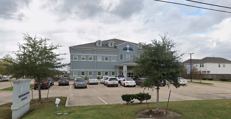 Exterior view of a gray-blue senior care building with cars parked in front