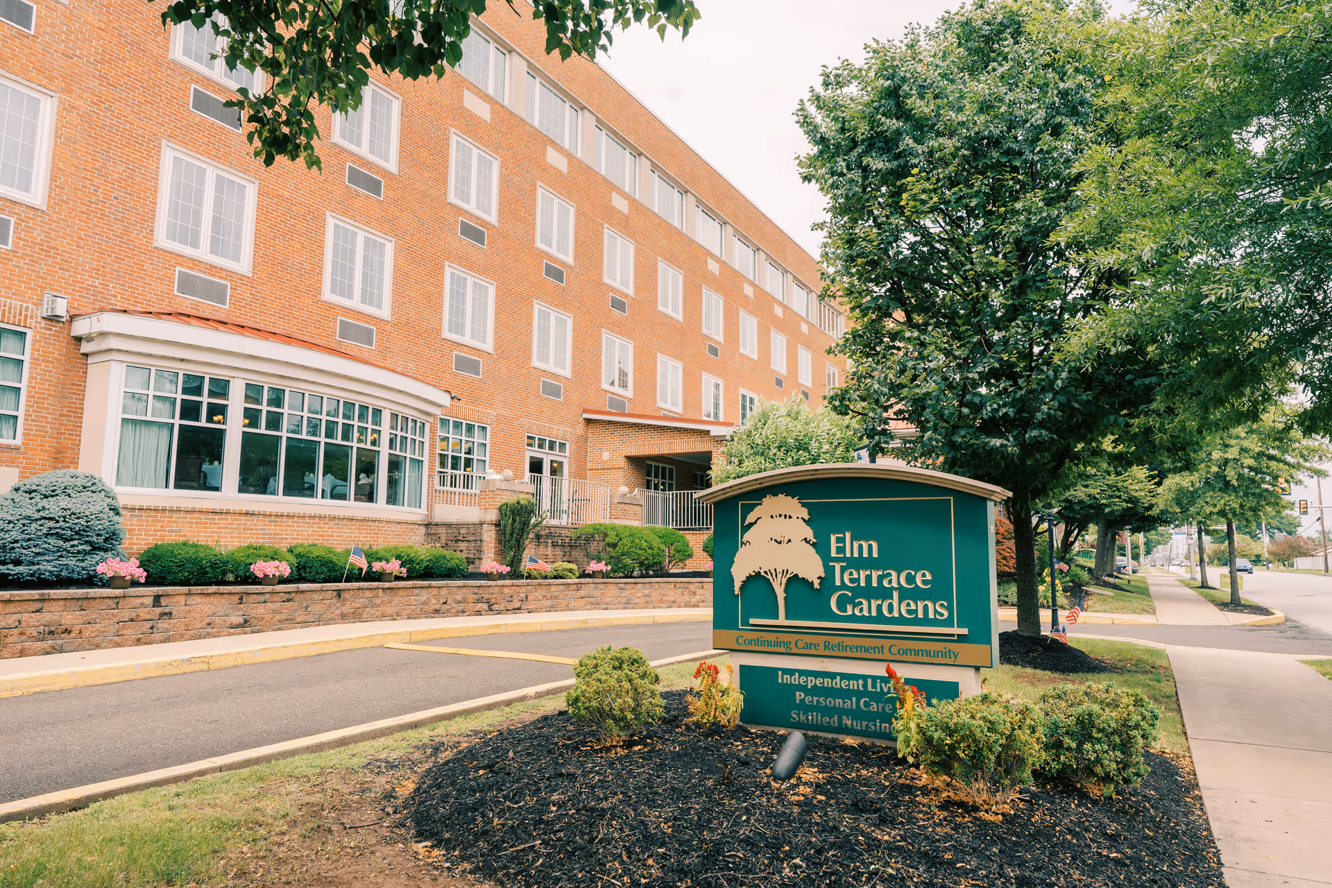 Brick senior living facility with Elm Terrace Gardens sign and landscaped front.