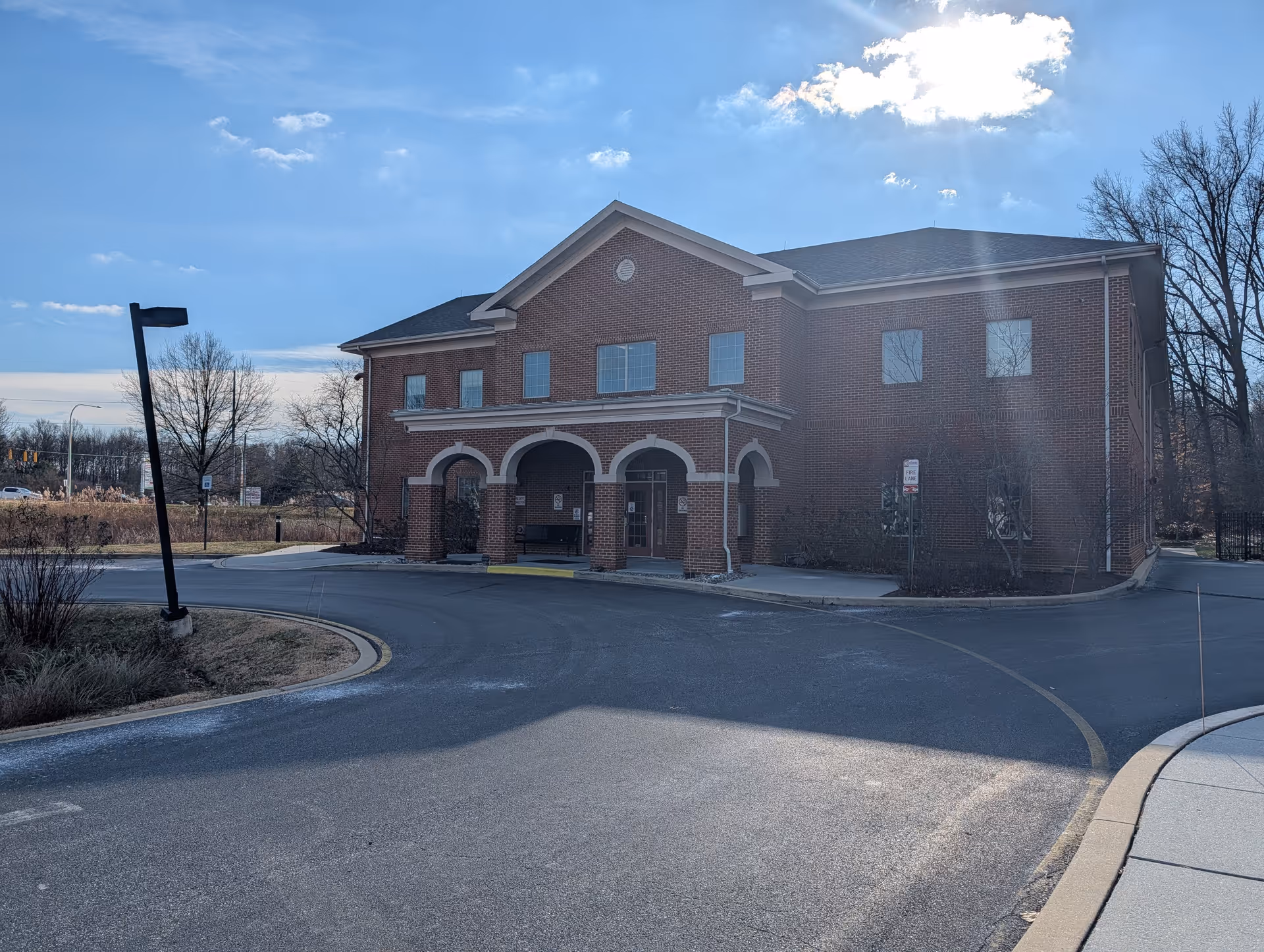 Brick two-story building with arched entrance, circular driveway, and bare trees surrounding.