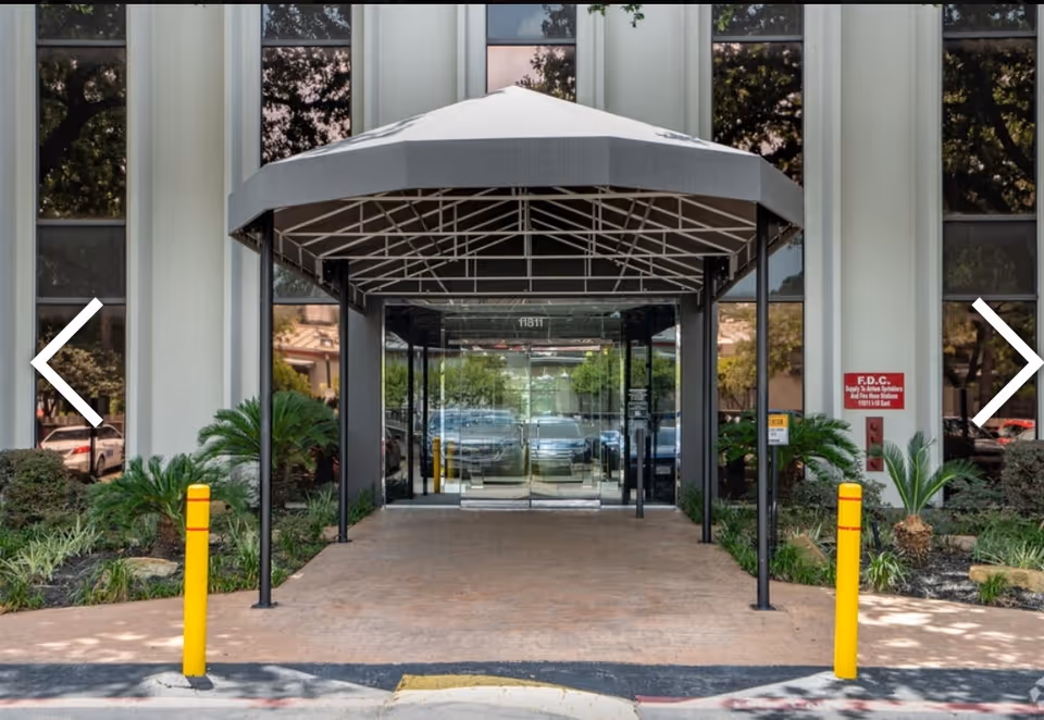 Front entrance of a modern building with glass doors, walkway, and a large canopy.