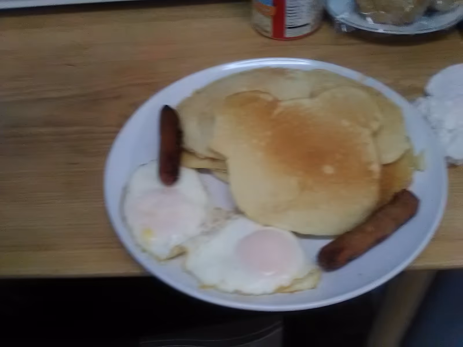 Breakfast plate with eggs, sausage, and a biscuit on a wooden table.