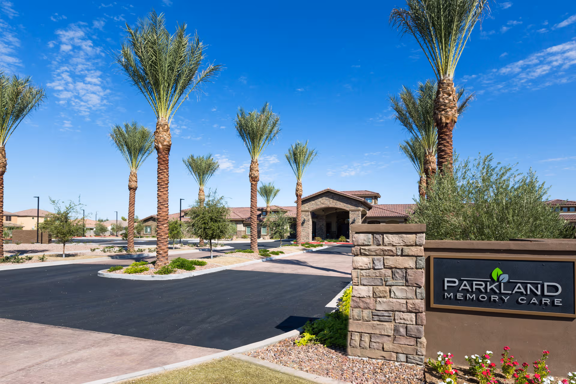 Entrance of Parkland Memory Care with palm trees, stone sign, and a curved driveway.