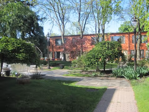 Brick senior living building with a landscaped courtyard and paved walkway.