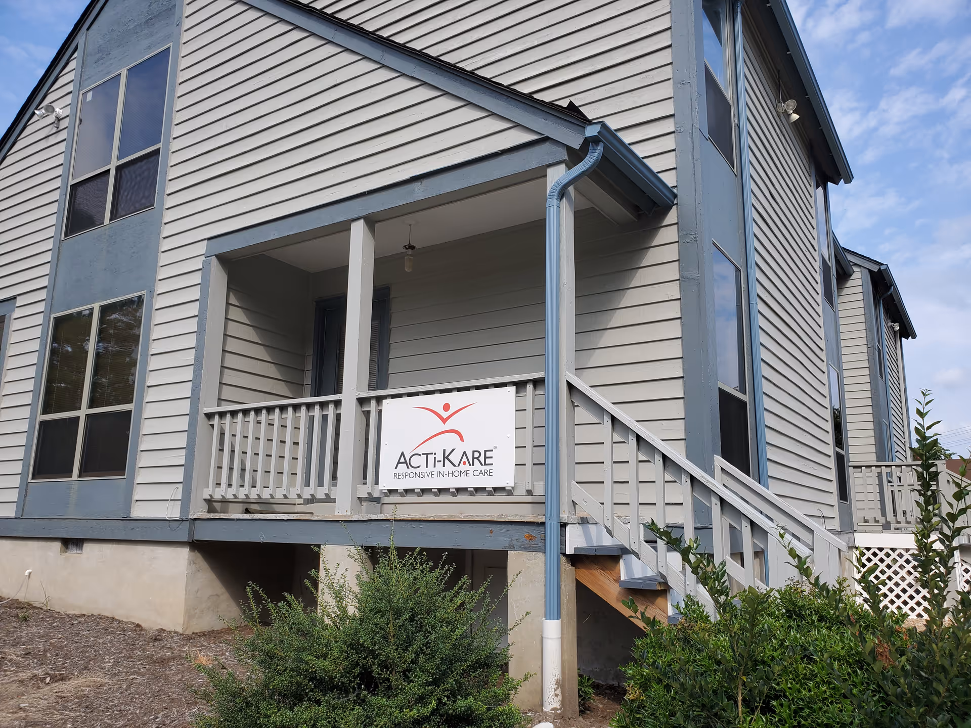 Exterior of a two-story Acti-Kare senior care building with a front porch sign.
