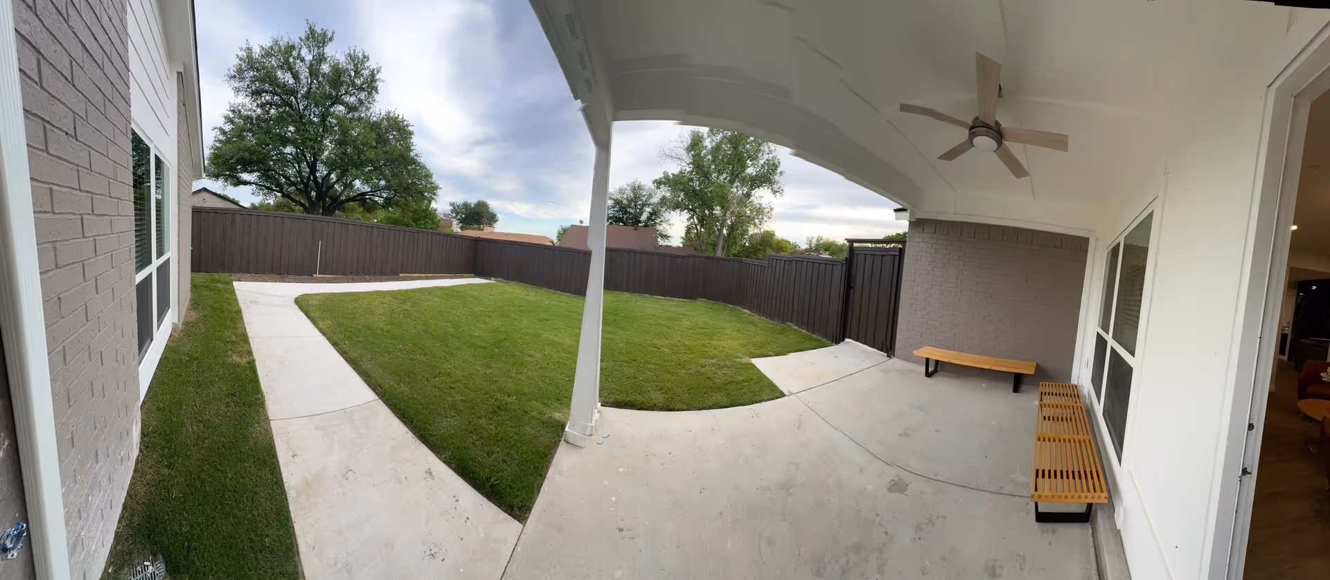 Covered patio with benches, a ceiling fan, and a grassy fenced backyard.