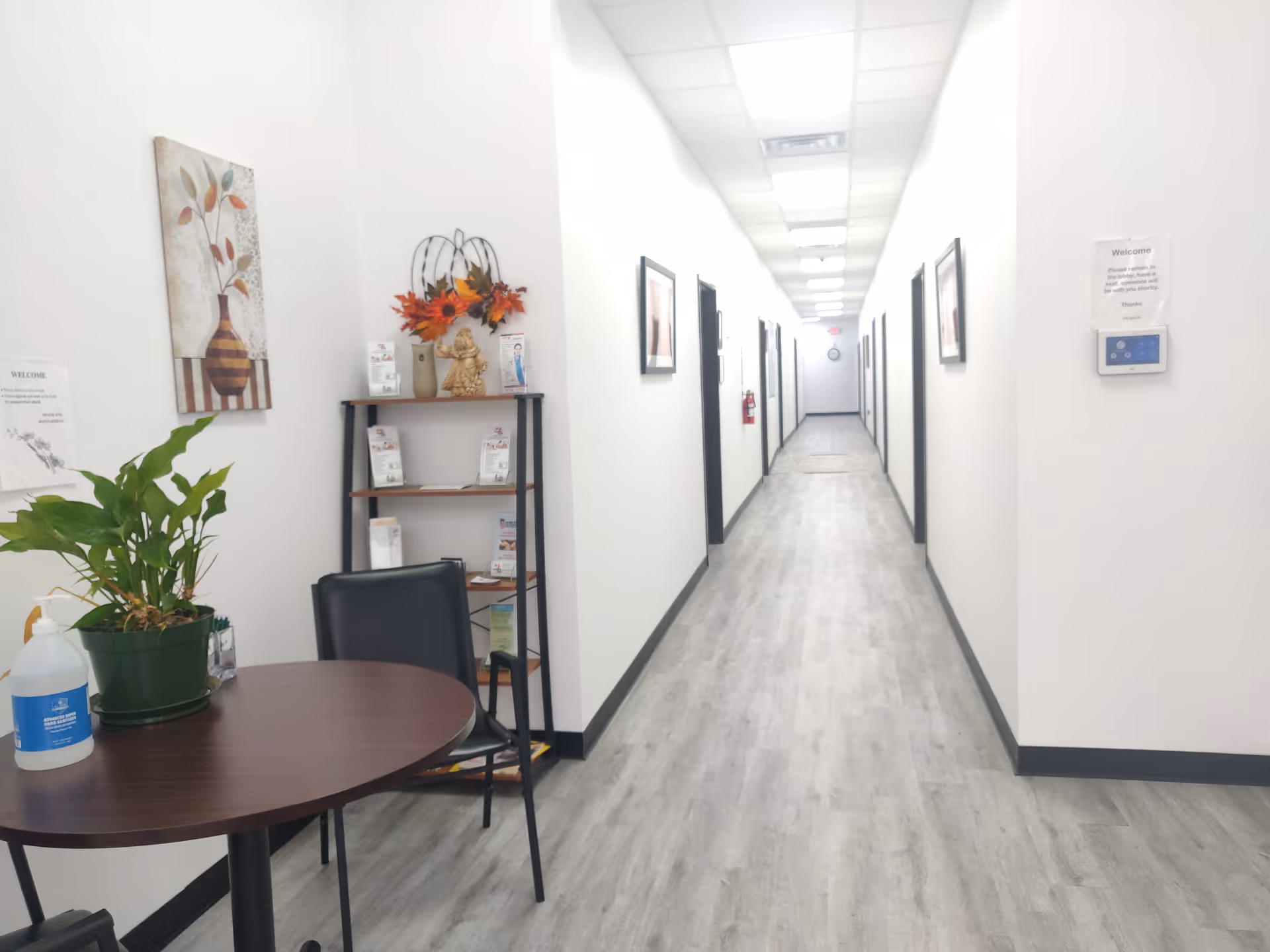 White hallway inside a senior living facility with a round table and plants.