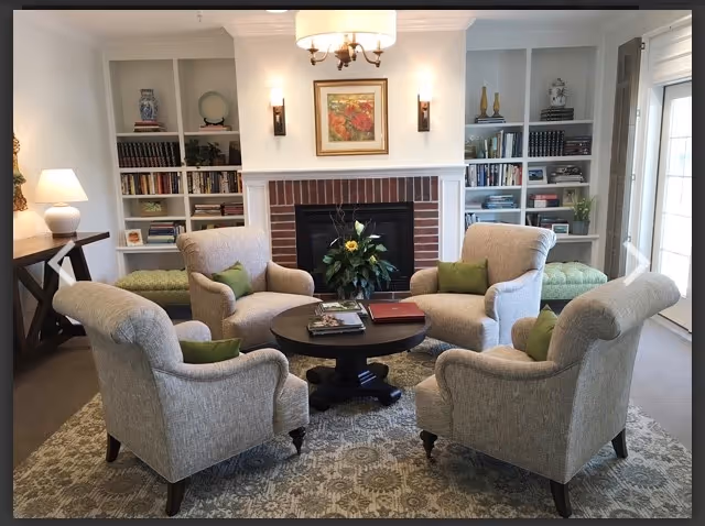 Cozy living room with four beige armchairs around a round coffee table near a fireplace.