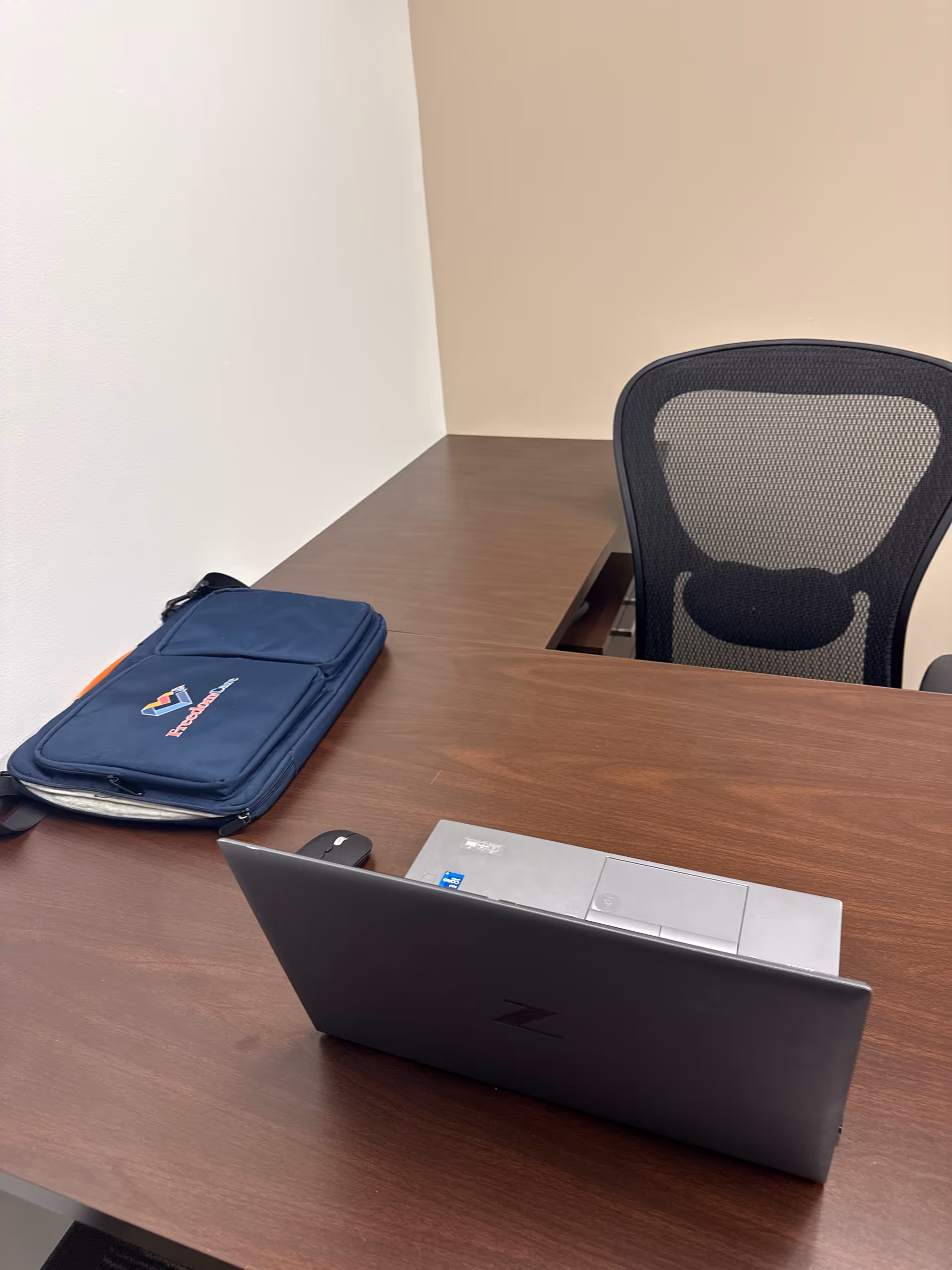 Desk with laptop and a blue FreedomCare bag in an office setting.