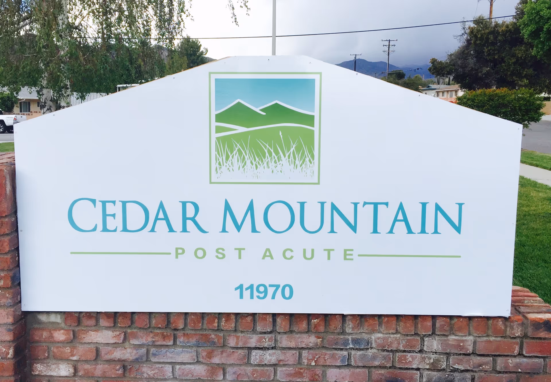 Outdoor sign reading Cedar Mountain Post Acute with mountain graphic on brick base.