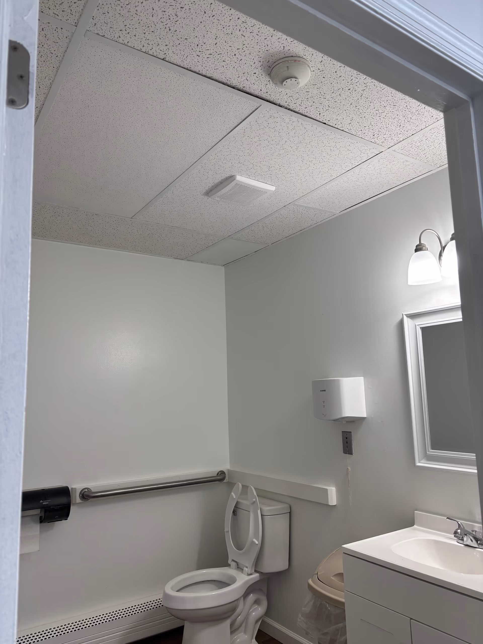 ADA-compliant bathroom with toilet, sink, mirror, and grab bar in a senior facility.
