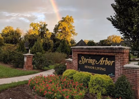 Exterior entrance sign for Spring Arbor Senior Living with landscaped grounds and a rainbow.