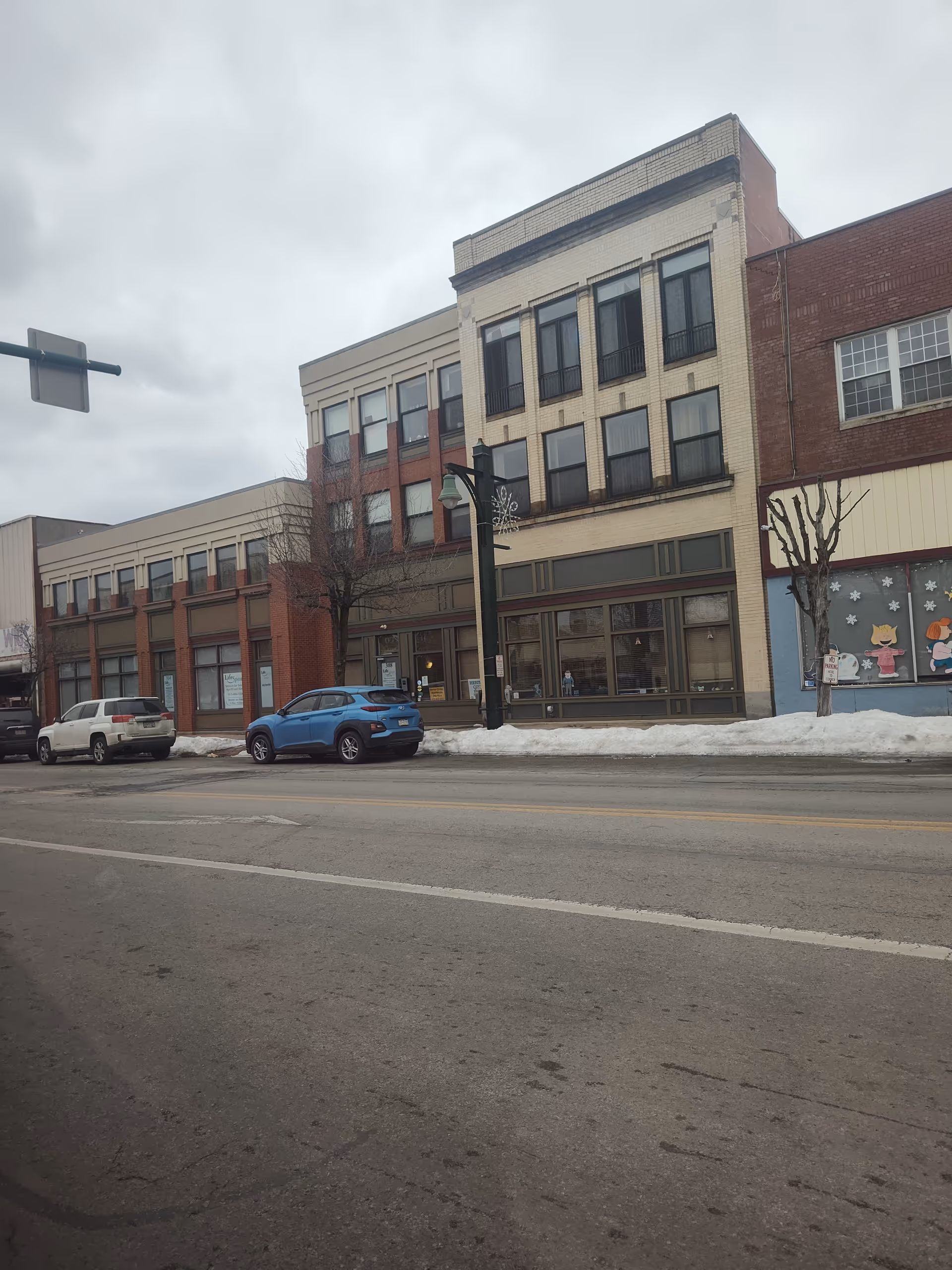 Street view of a brick, multi-story building with large storefront windows and parked cars.
