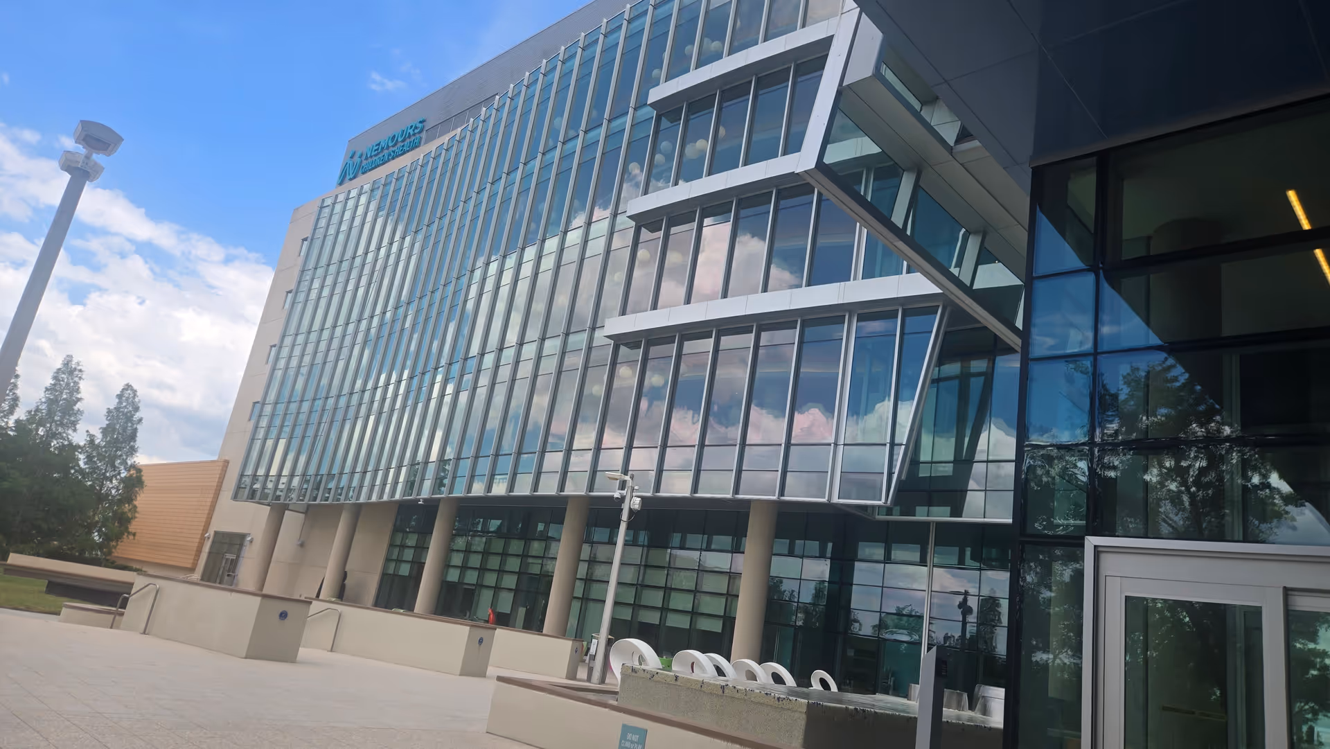 Modern glass-front medical building with Nemours signage and angular overhangs under a blue sky.