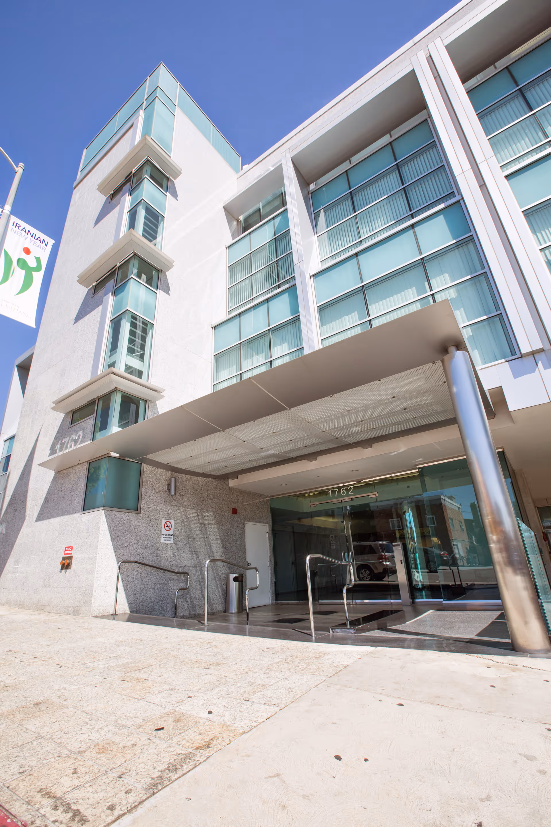 Modern multi-story senior facility entrance with glass facade and covered drop-off area.
