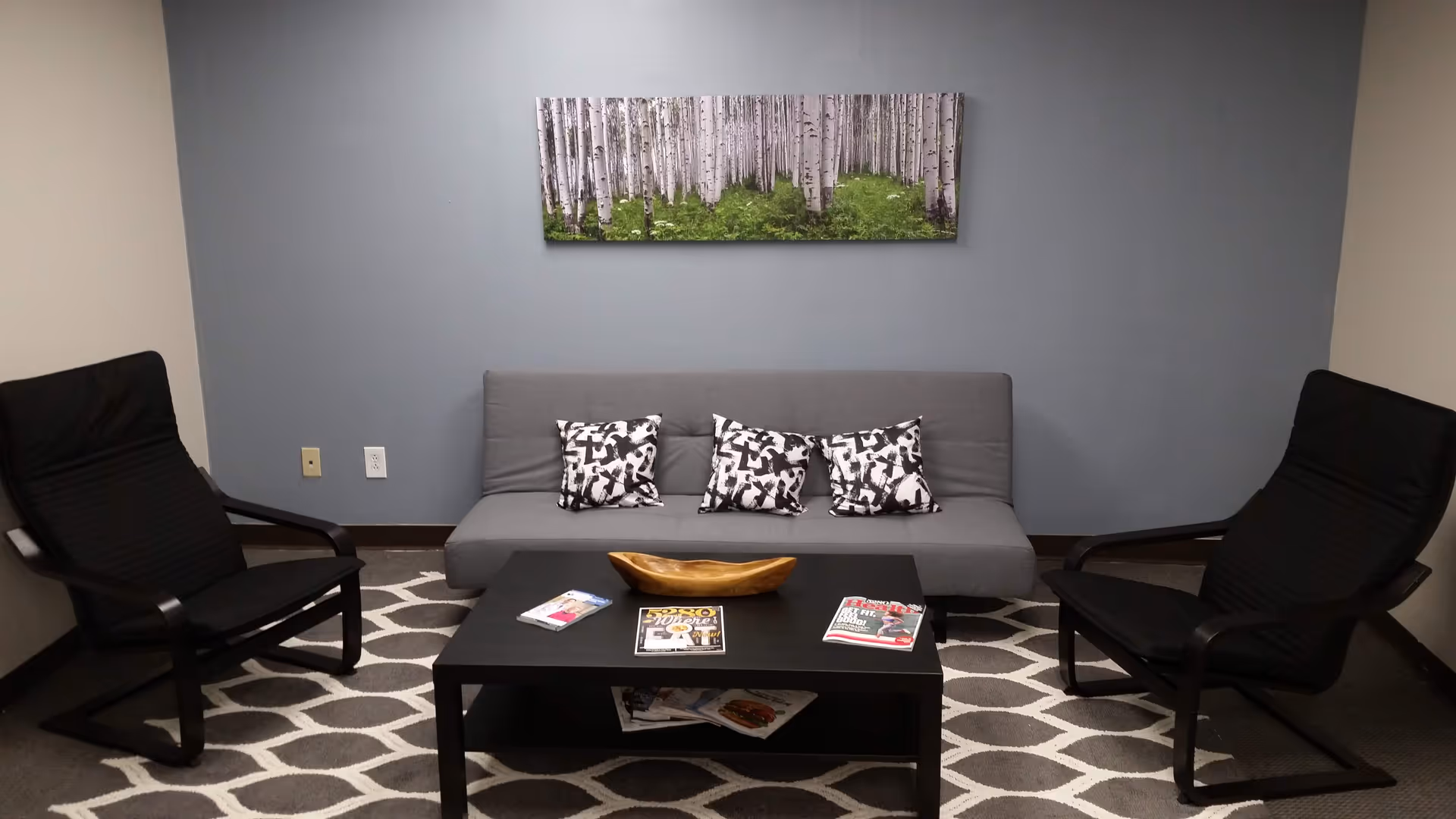 A gray sofa with two black chairs around a coffee table in a modern lounge area.