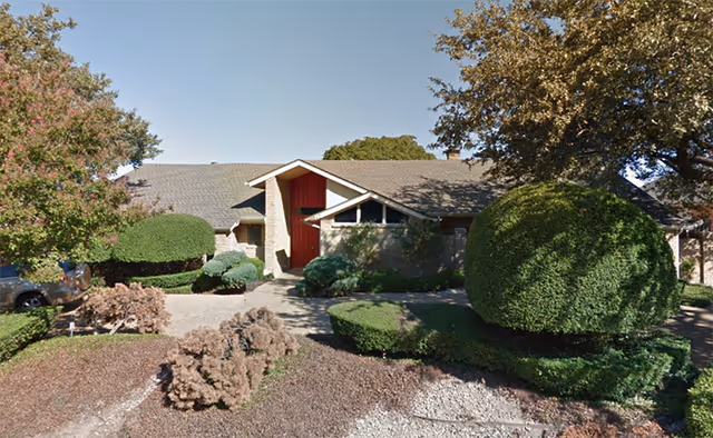 Front view of a single-story senior living facility with manicured shrubs and a red entrance.
