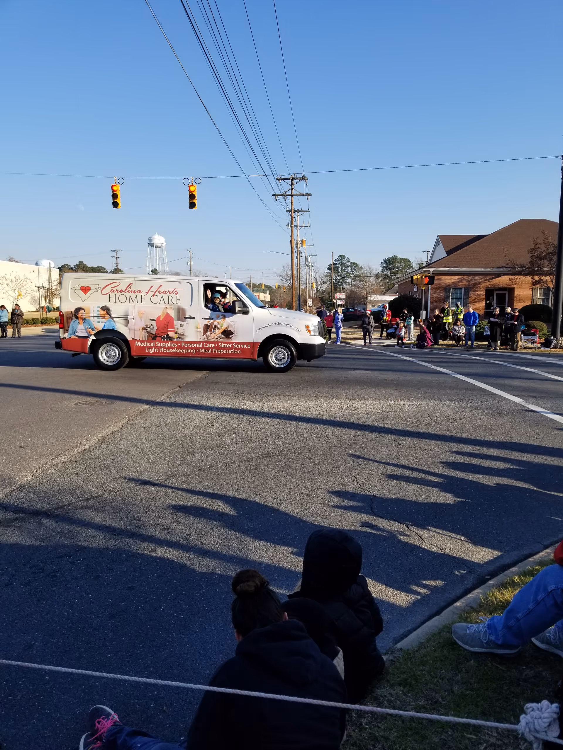 Carolina Hearts Home Care van drives through a street as spectators watch.
