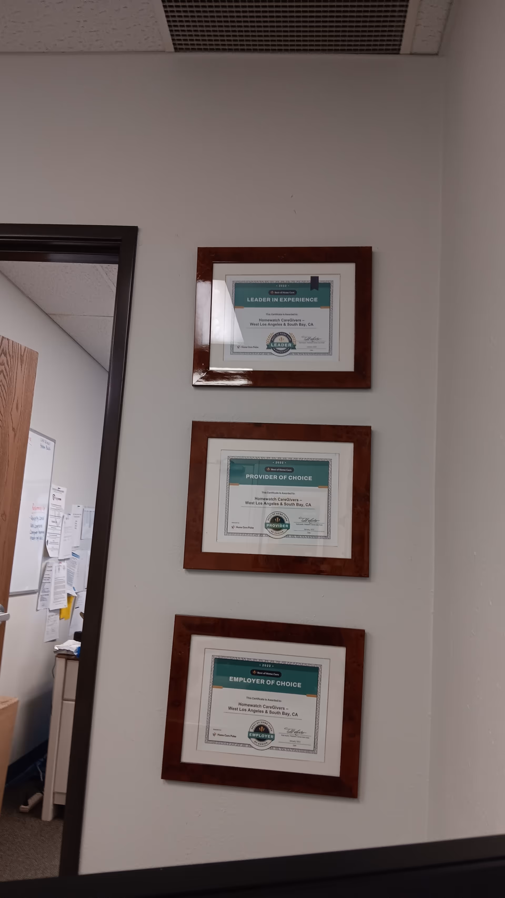 Interior wall with three framed certificates beside an open door in an office area.