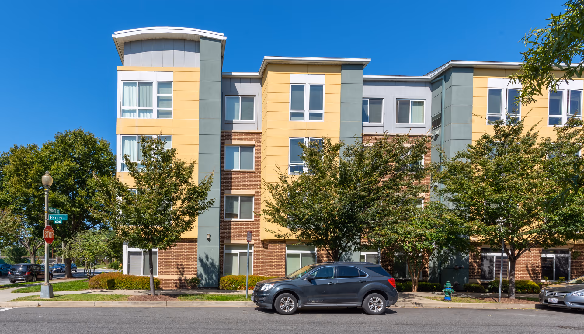 Modern multi-story senior living building with colorful facade, trees, and parked cars.