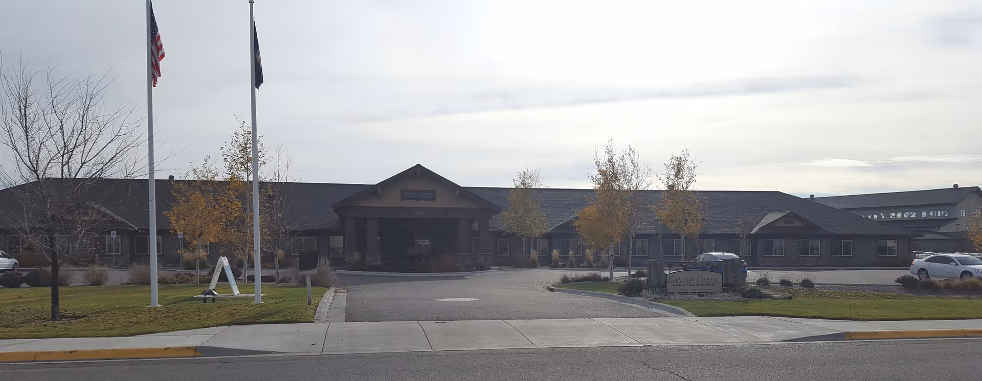 Exterior view of Canyon Creek Memory Care Community building front with flags and landscaping.